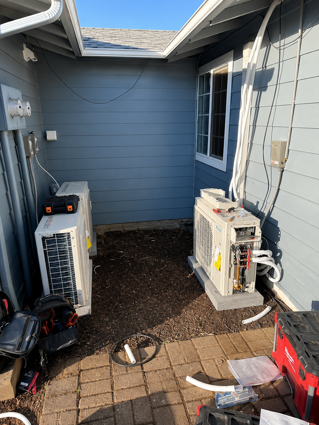 Narrow outdoor side yard with two air conditioner units against blue house siding and brick pavers on the ground