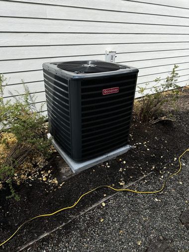 Outdoor air conditioner unit beside a house on a concrete pad, with weeds and a yellow cord nearby