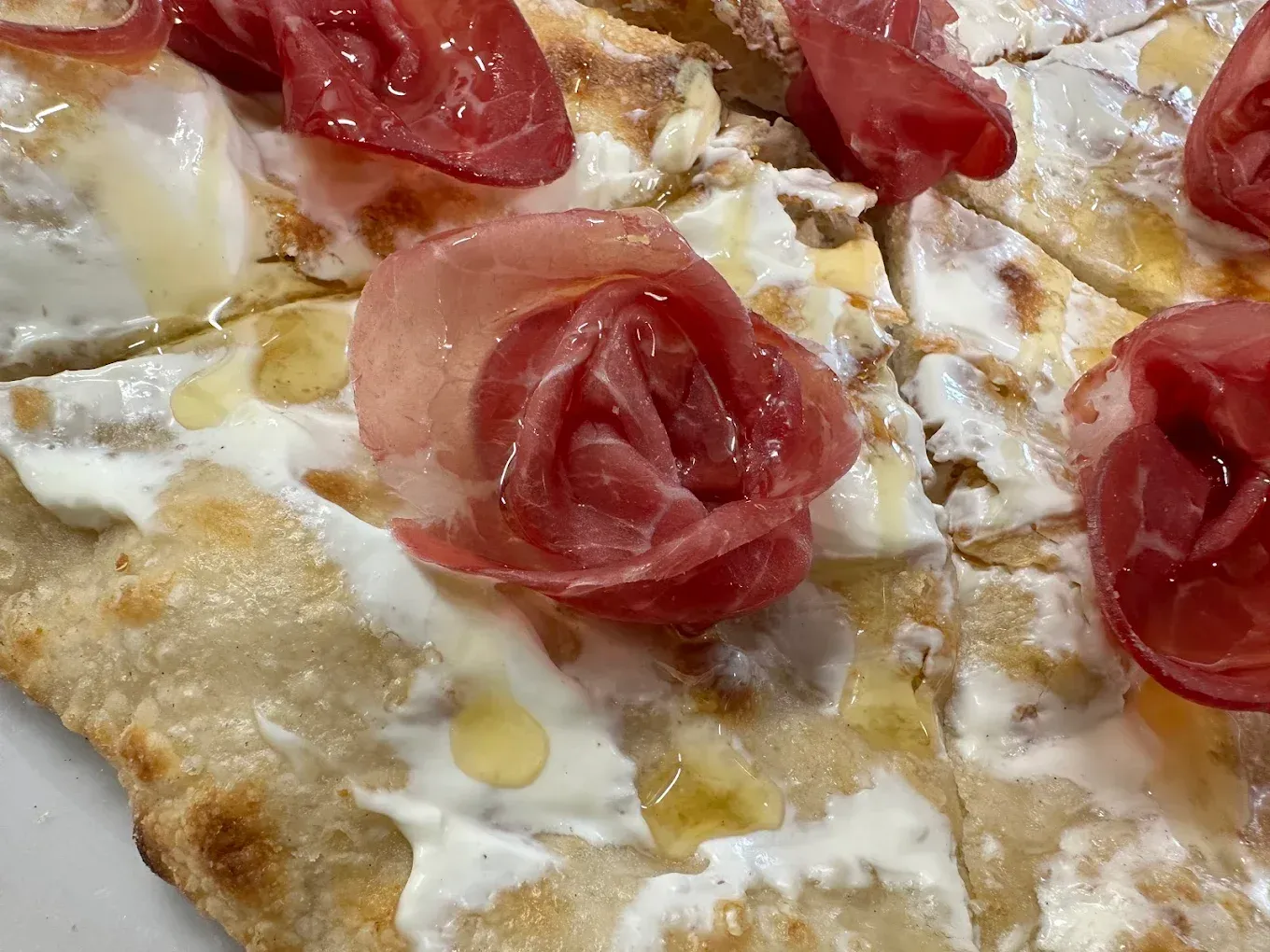 Primo piano di una pizza con prosciutto e formaggio su un piatto bianco.