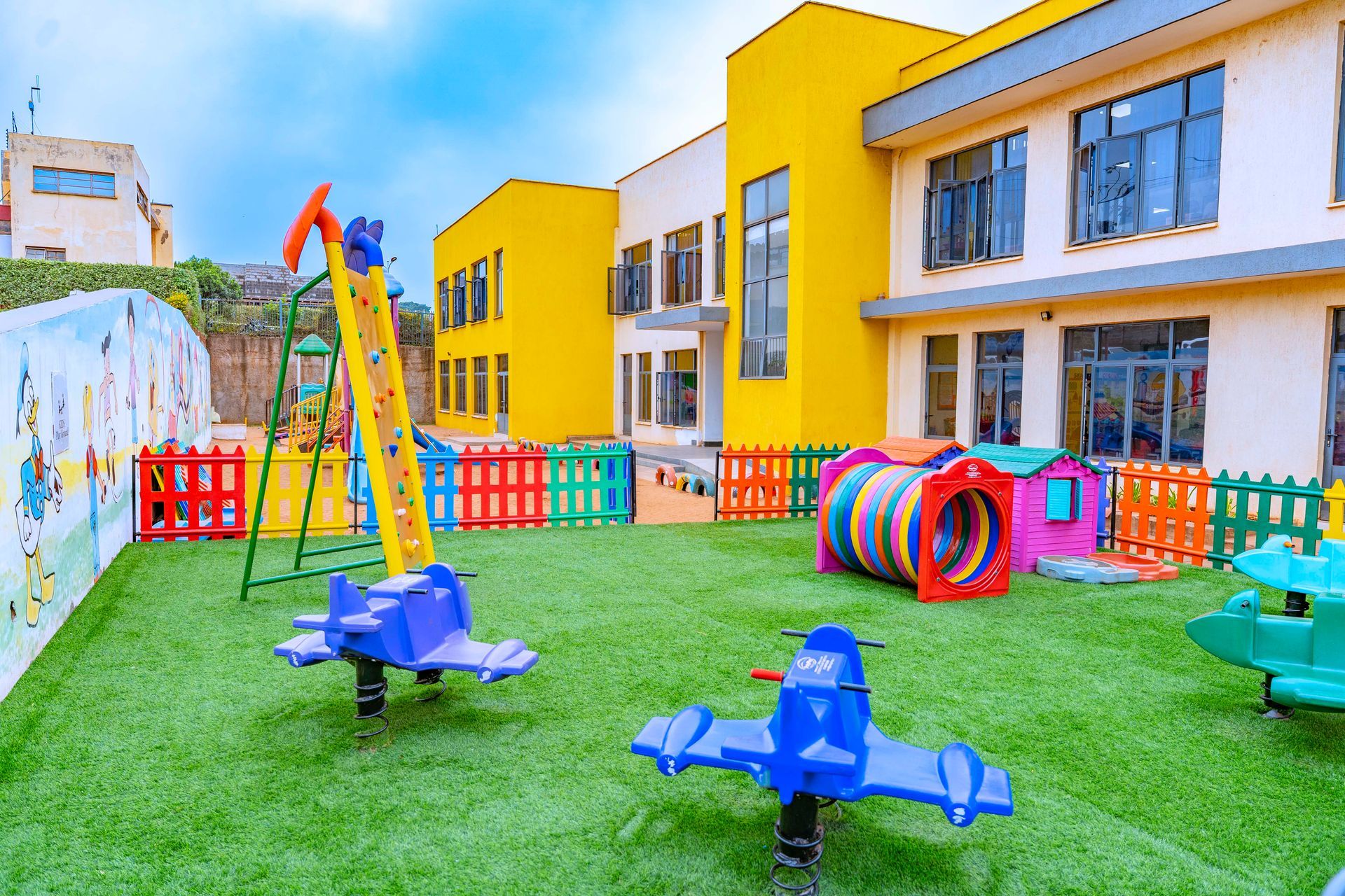 A playground with swings and a mural on the wall in front of a building.