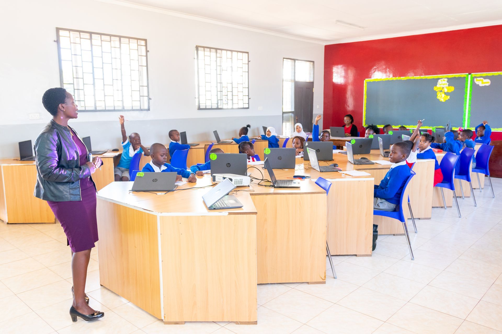 A woman is standing in front of a classroom full of children using laptops.