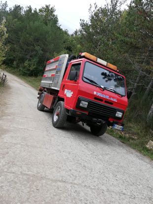 Camion fuoristrada rosso che percorre una strada sterrata, con alberi sullo sfondo.