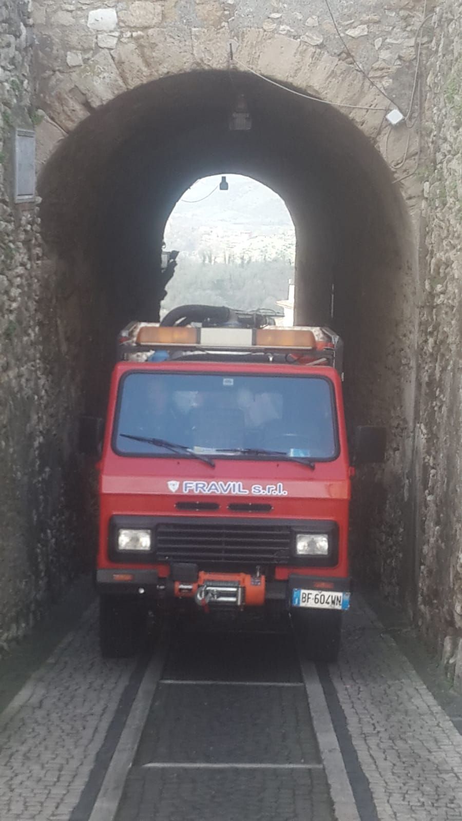 Un camion rosso attraversa un arco di pietra. Sul davanti c'è la scritta FRAVIL. 