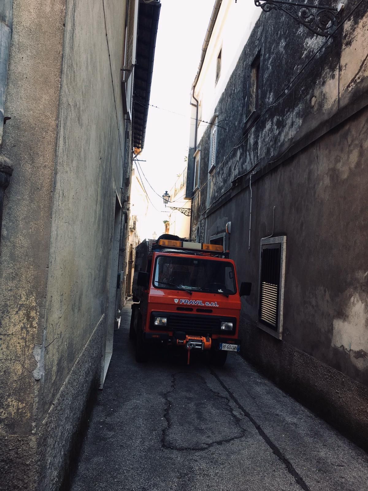 Camion Fravil rosso in uno stretto vicolo tra edifici rovinati dal tempo; Italia.