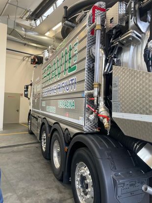 Un grande camion argentato con fiancate romboidali e scritta verde, parcheggiato al chiuso.