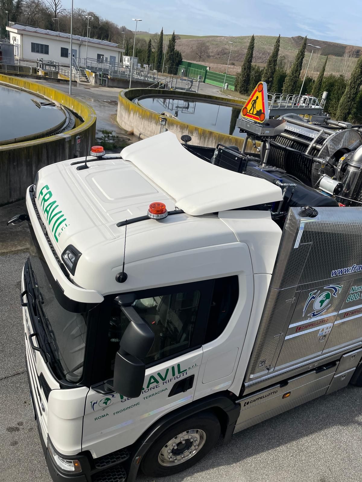 Camion bianco Fravil presso un impianto di trattamento delle acque. Sullo sfondo si vedono vasche circolari ed edifici.