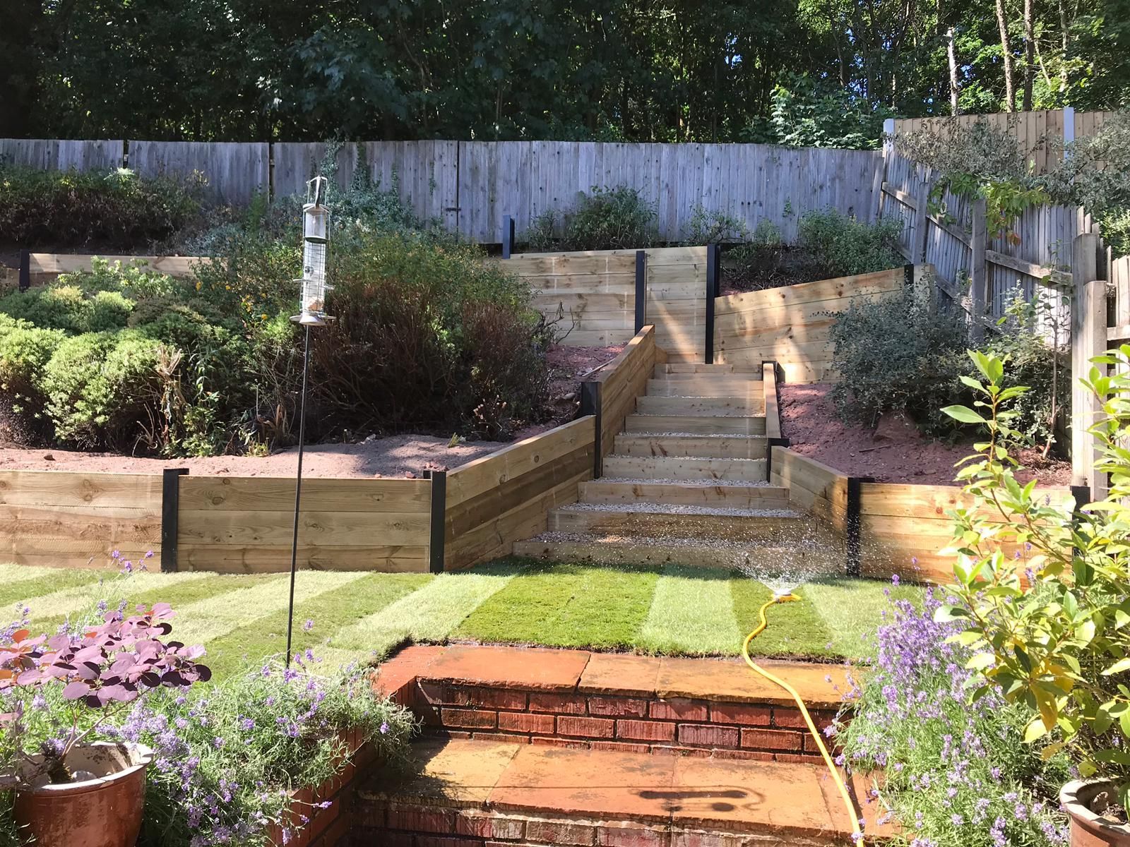 Terraced backyard garden with stone steps, retaining walls, and colorful plants in sunlight