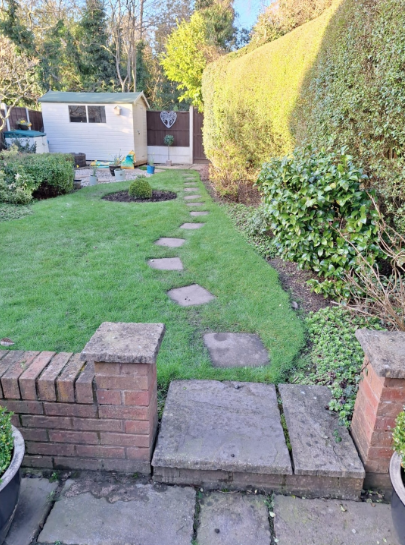 Garden path with stepping stones leading to a small shed, bordered by grass and hedges.