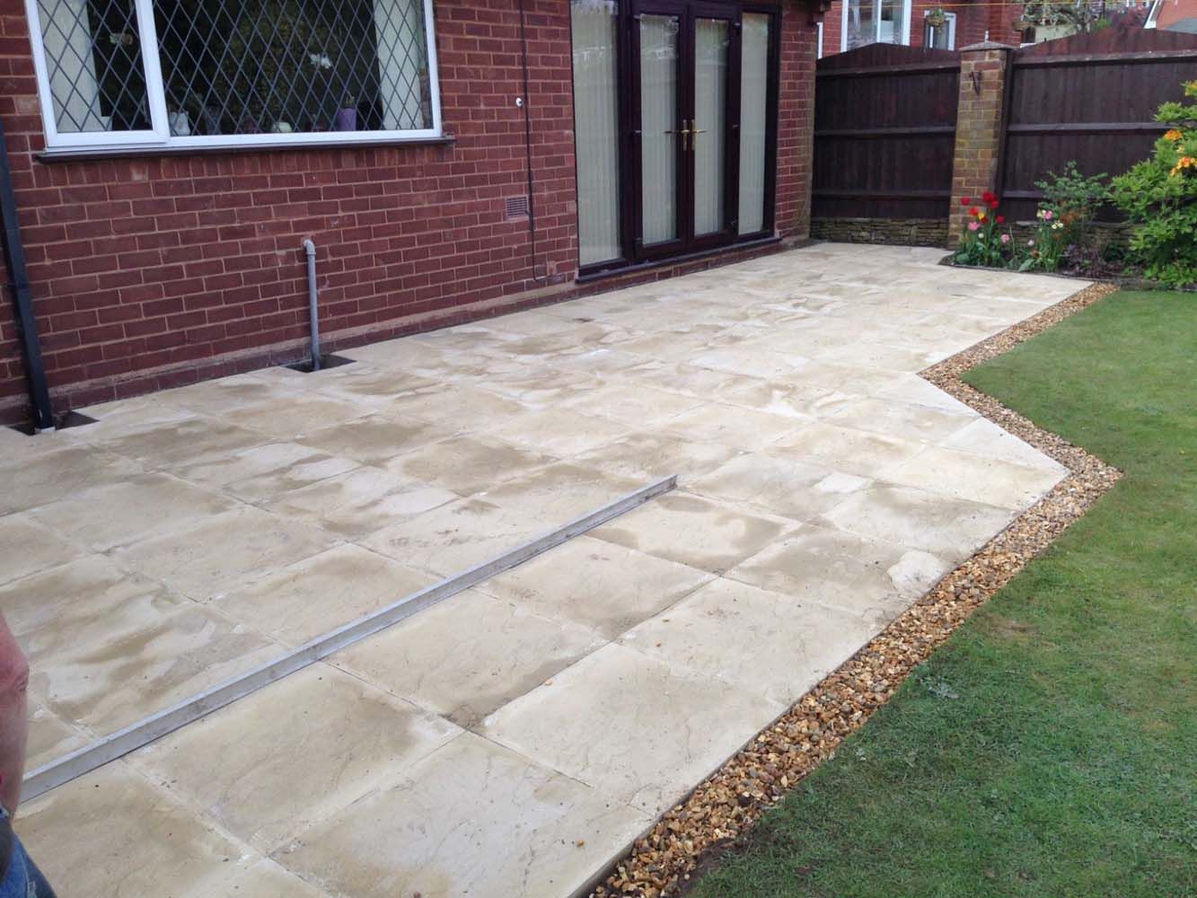 Stone patio beside a brick house, with a lawn edge and gravel border.