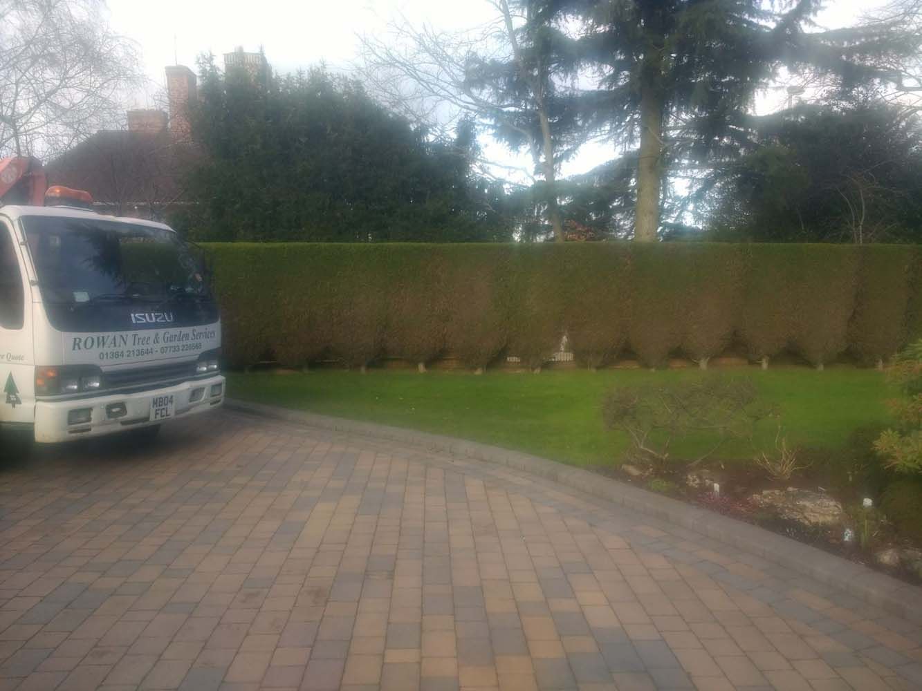 White van parked on a brick driveway beside a hedge and green lawn under overcast skies