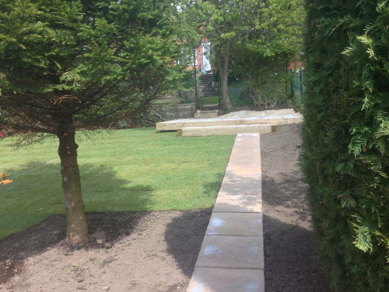 Garden path leading to a stone bench beside a grassy lawn and trees