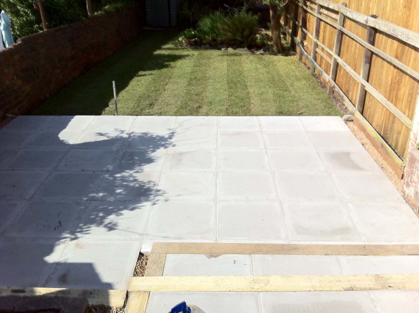 Backyard with newly paved gray patio, grassy lawn, and wooden fence along the right side