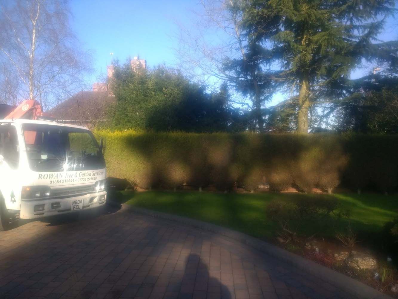 White truck parked on a brick driveway beside a hedge and trees in bright sunlight