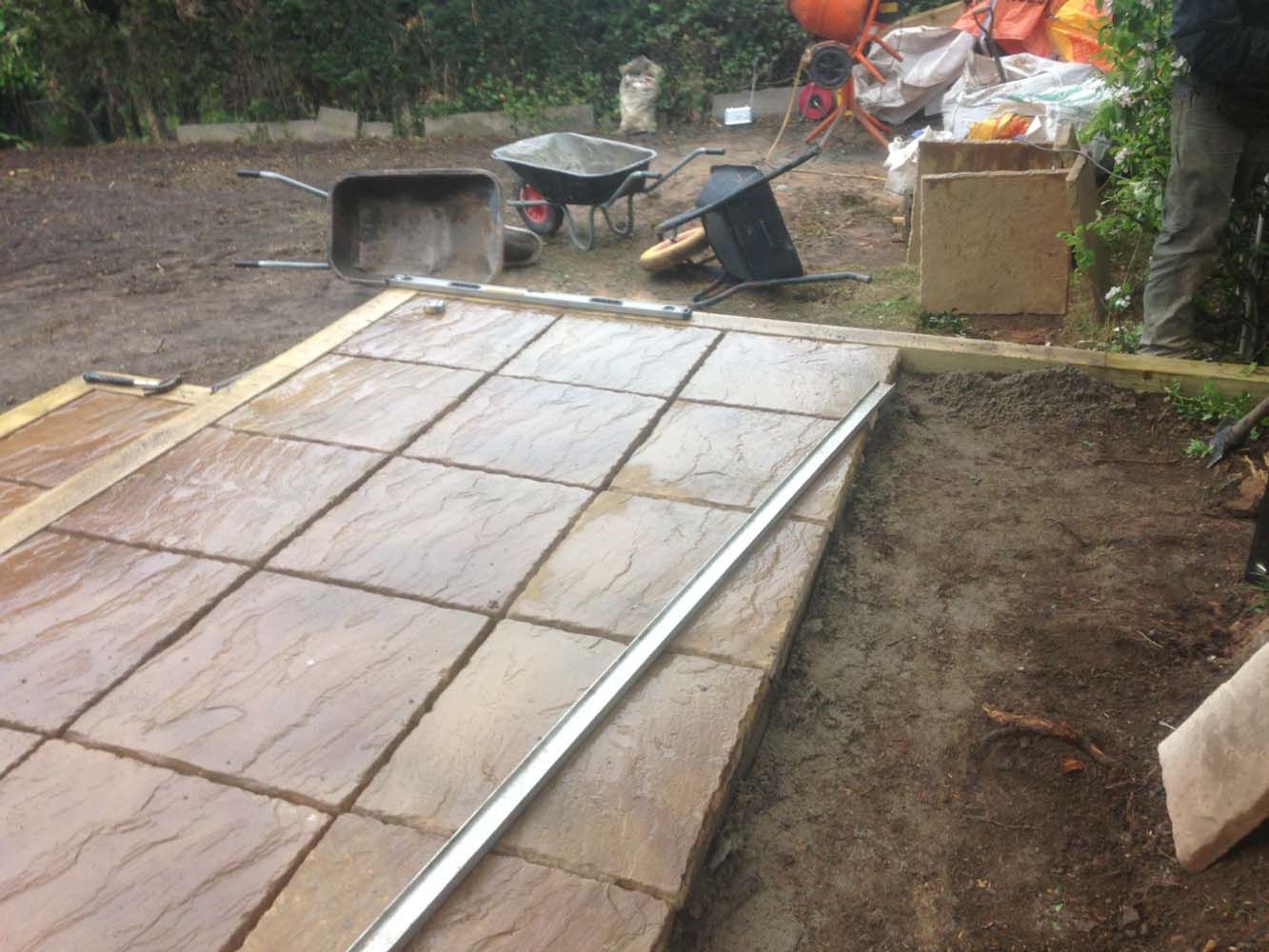 Concrete ramp under construction in a muddy outdoor yard with tools and debris nearby