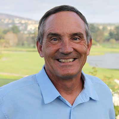 Smiling man in a blue shirt stands outdoors against a golf course backdrop.