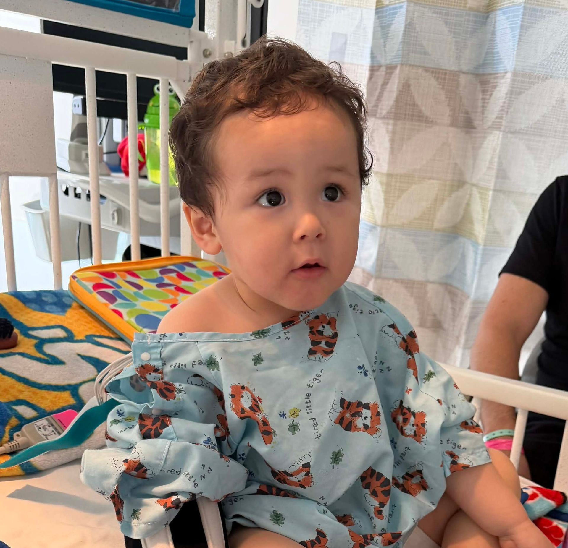 A child in a hospital bed wearing a tiger-print gown and looking to the side.
