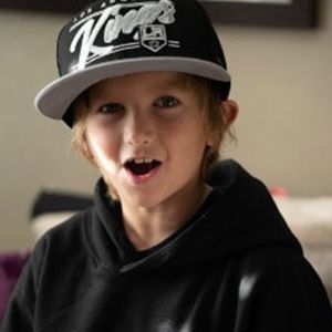 Young boy with Kings baseball cap smiles, wearing a black hoodie.