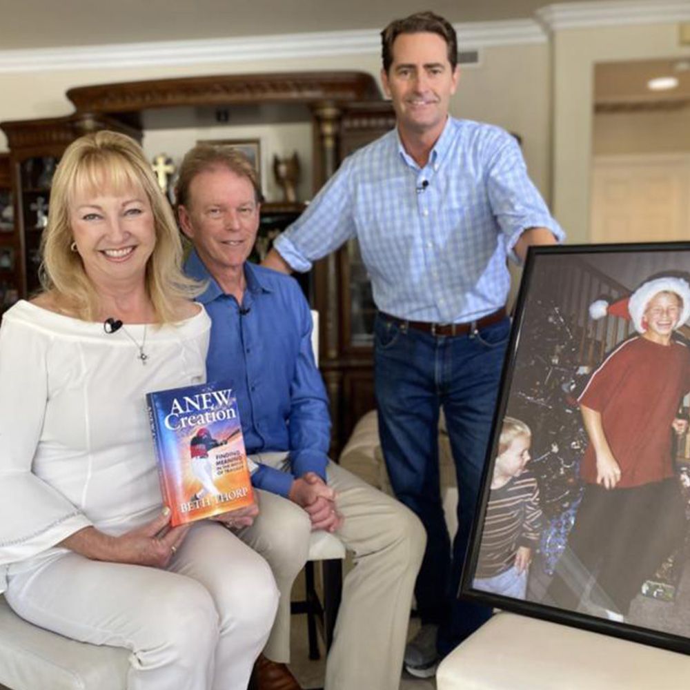 Family with a book, photo, and a smiling man in a blue shirt. Woman in white holding the book.