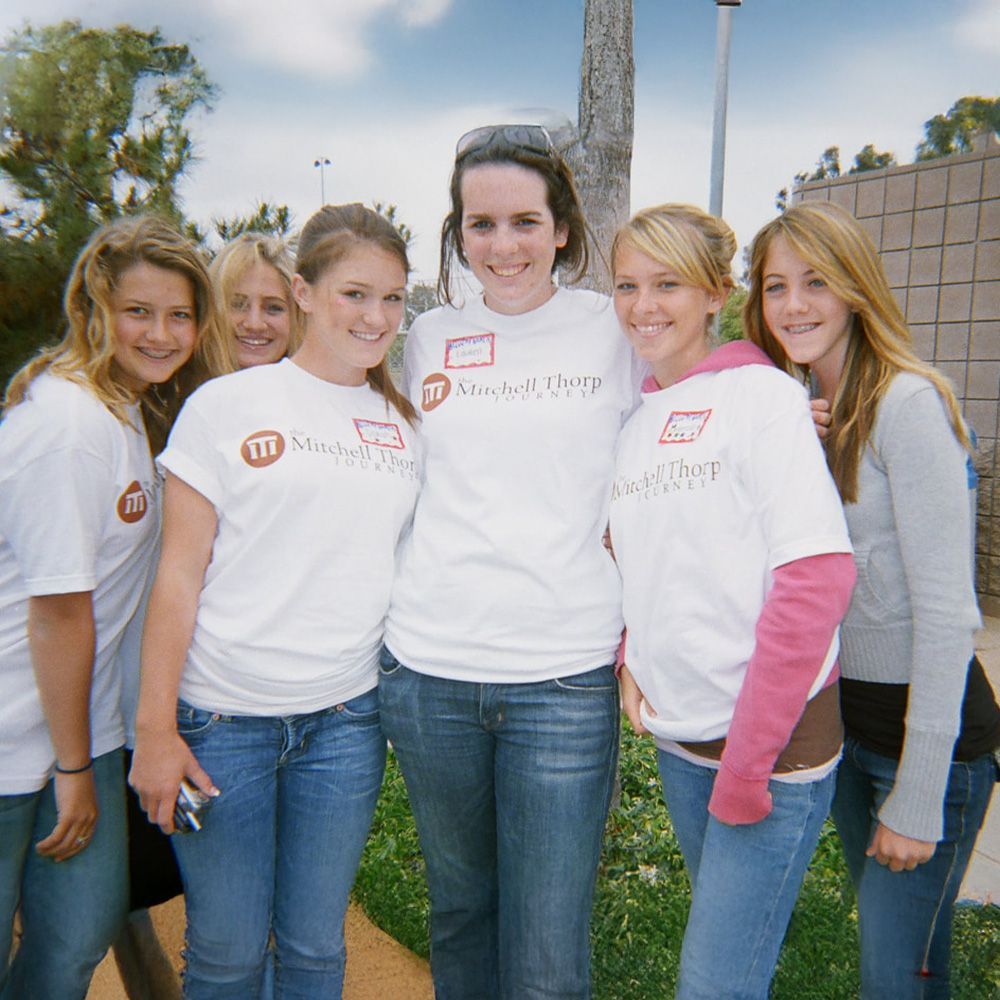 Group of young women in white t-shirts, blue jeans, and smiles pose outdoors.
