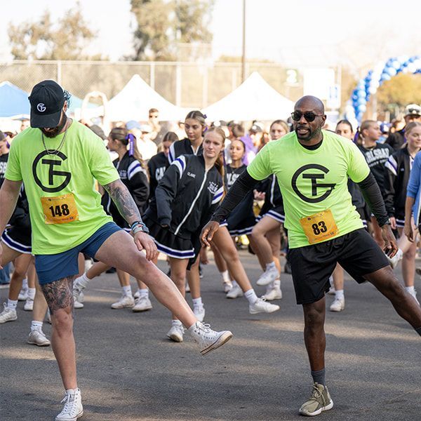 Two people in neon green shirts stretching, group of people in background.