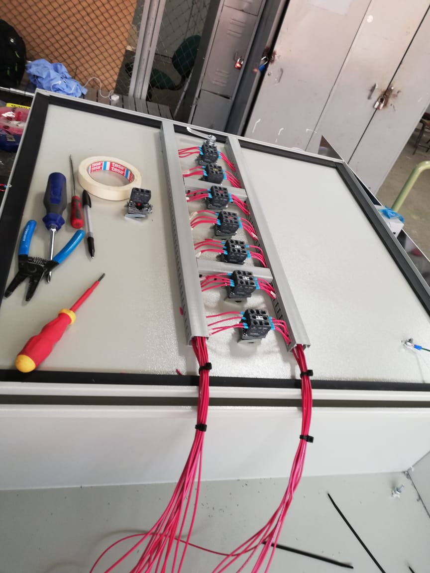 Panel de cableado eléctrico con cables rojos, conectores y herramientas.