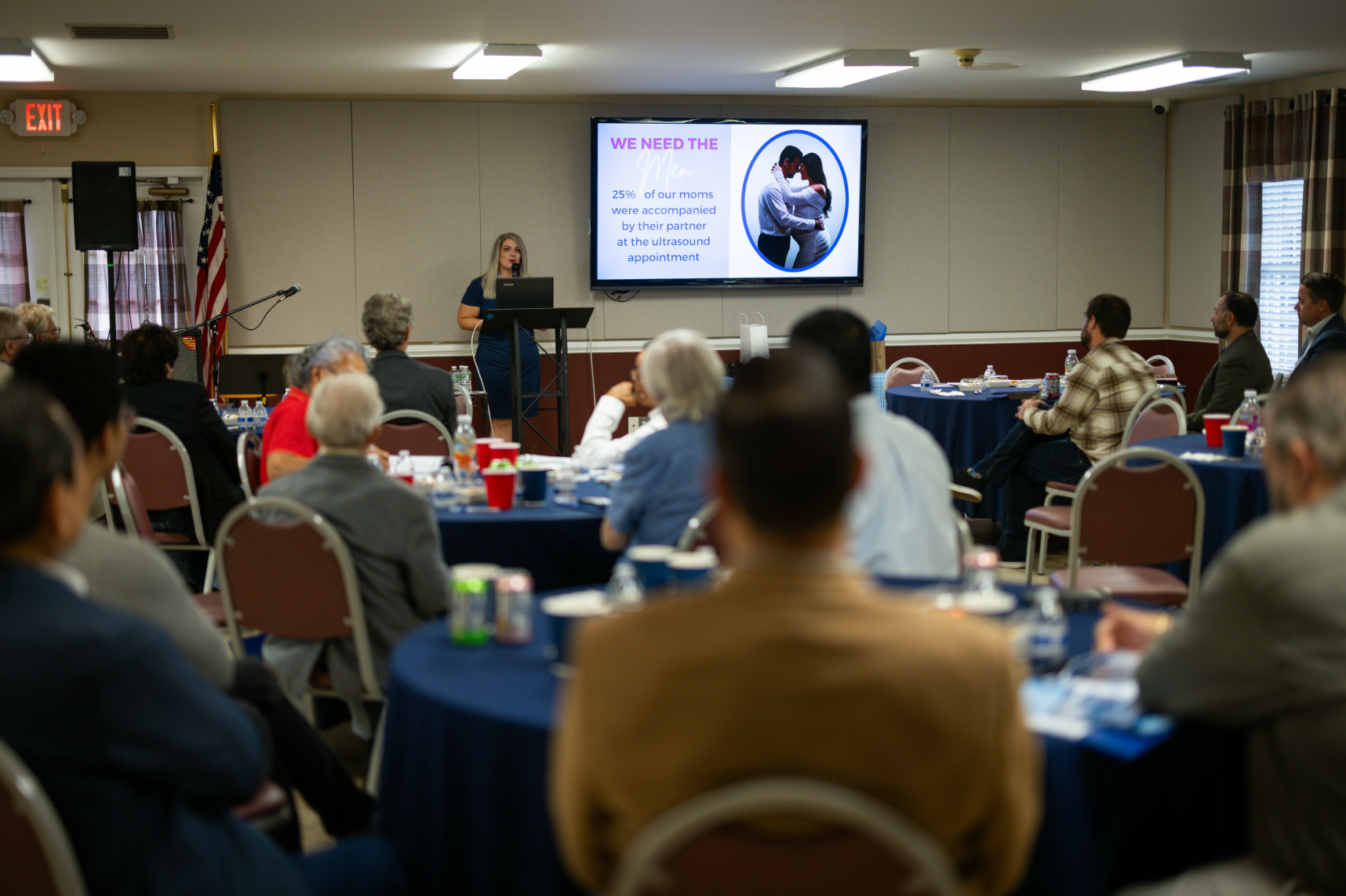 A group of people are sitting at tables in a room watching a presentation.
