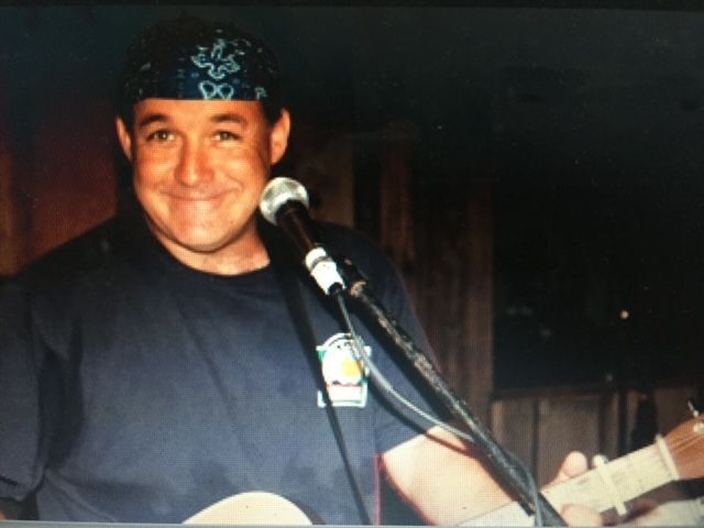 A man wearing a bandana is playing a guitar in front of a microphone
