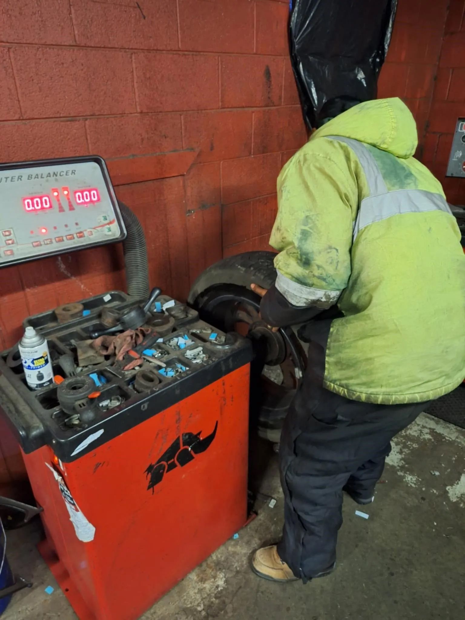 A man in a yellow jacket is working on a tire balancing machine.