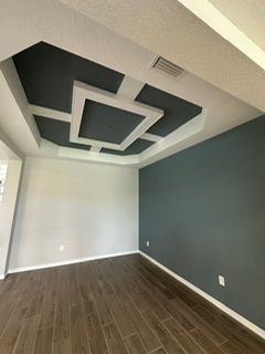 Person painting white trim around a window with a brush. A bucket of white paint is on the floor.