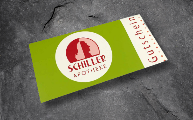 Ein Gutschein für die Schiller-Apotheke liegt auf einer grauen Fläche