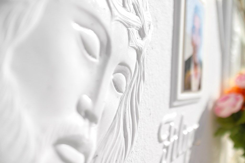 Un primo piano di una statua bianca raffigurante il volto di una donna su un muro.