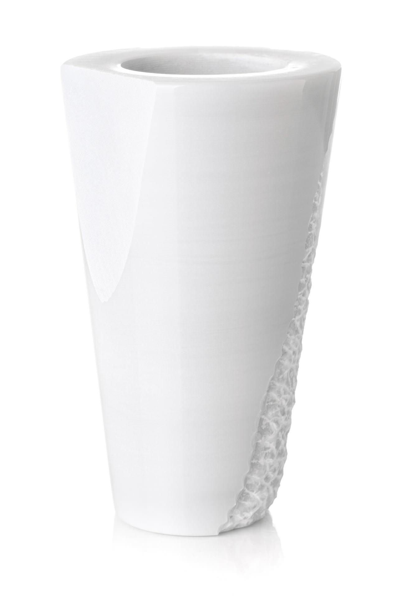 Un vaso bianco è appoggiato su una superficie bianca.