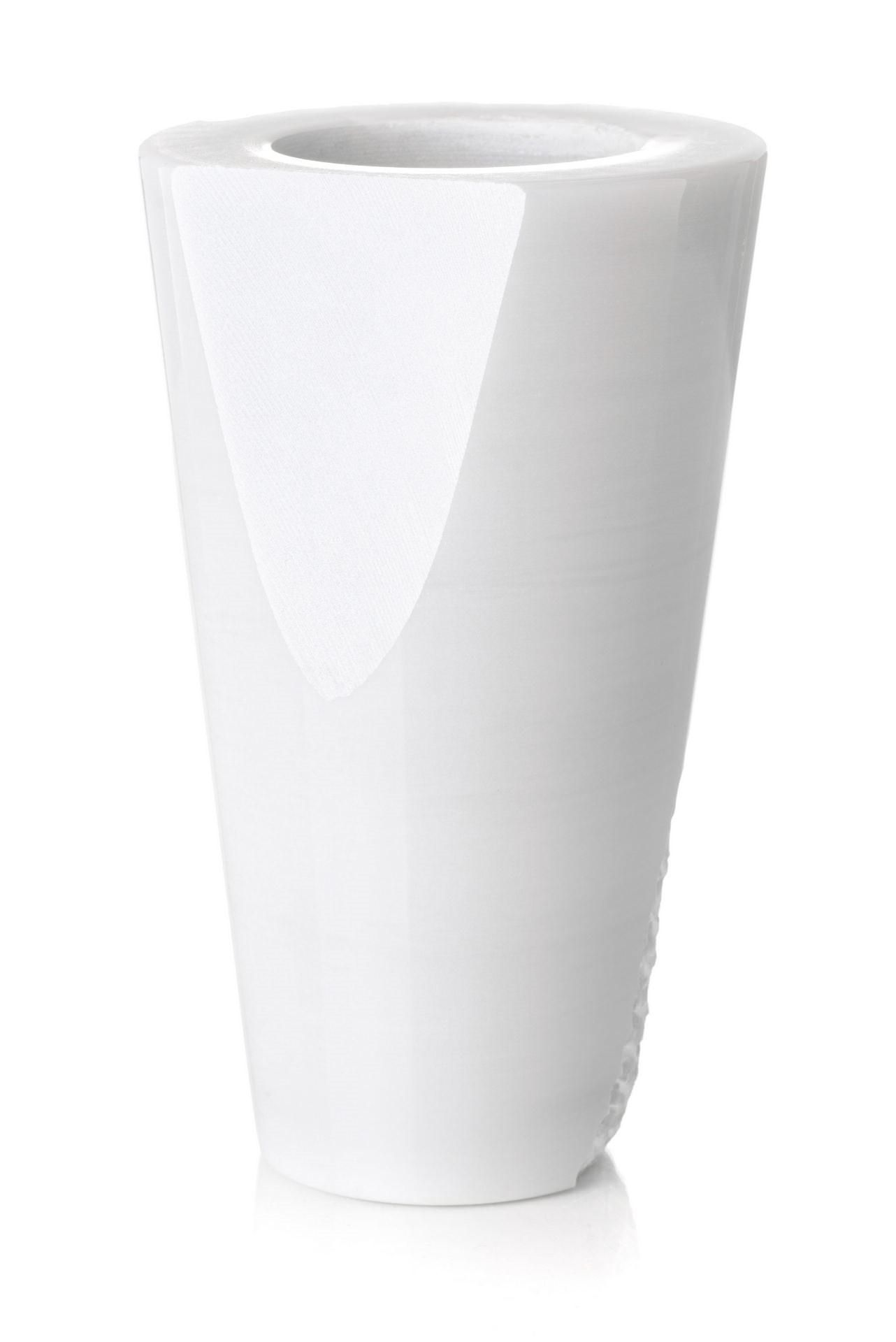 Un vaso bianco è appoggiato su una superficie bianca.
