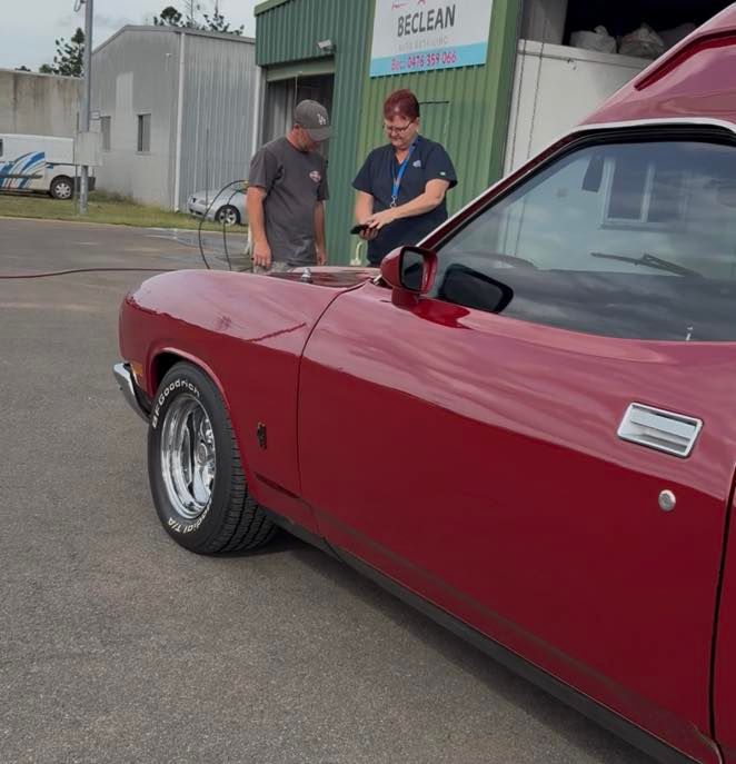 Two people standing beside a red classic car outside a building — Beclean Auto Detailing in Mareeba, QLD