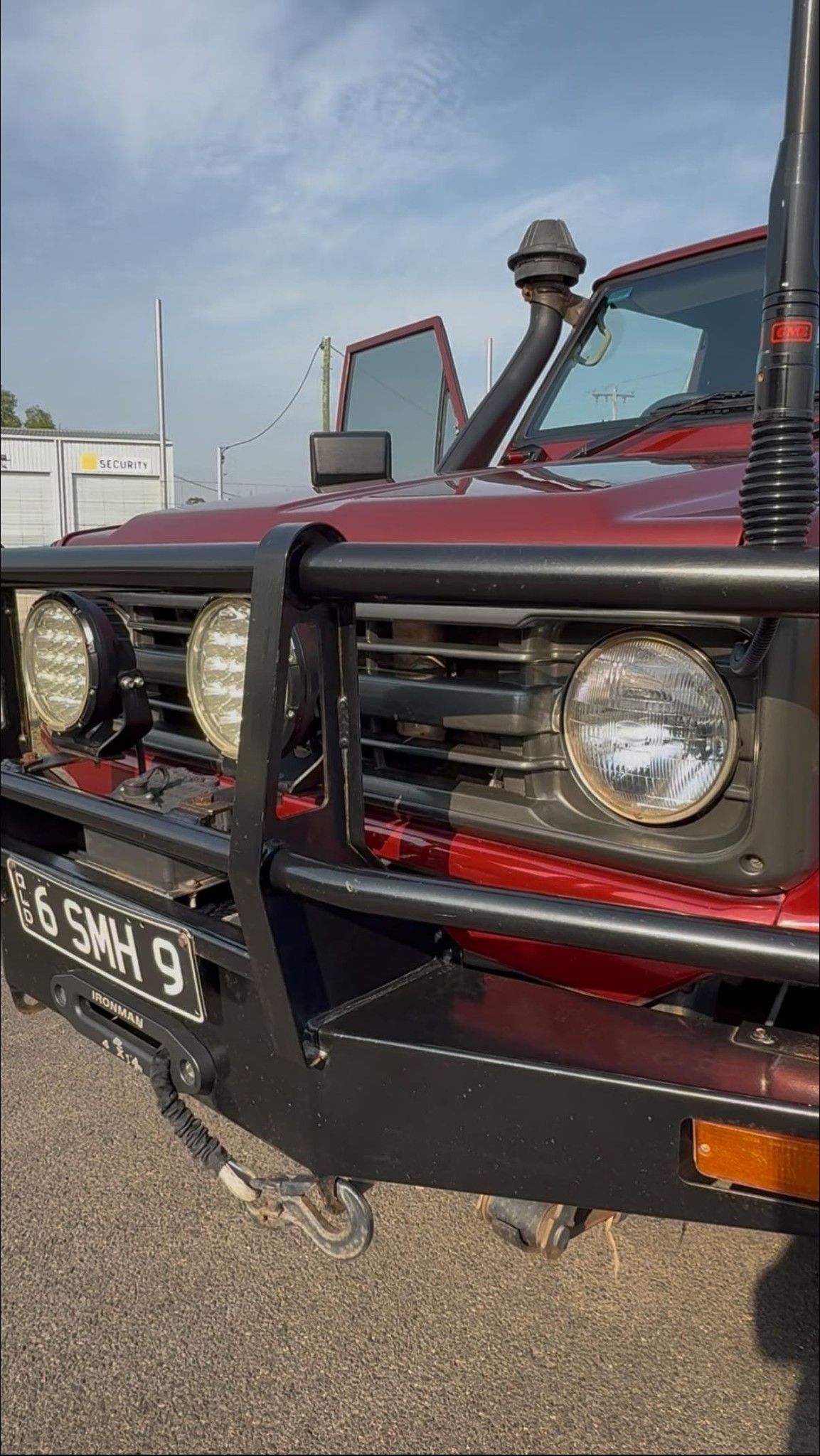 A close-up of a maroon off-road vehicle featuring a heavy-duty black bull bar, auxiliary lights, and a snorkel.