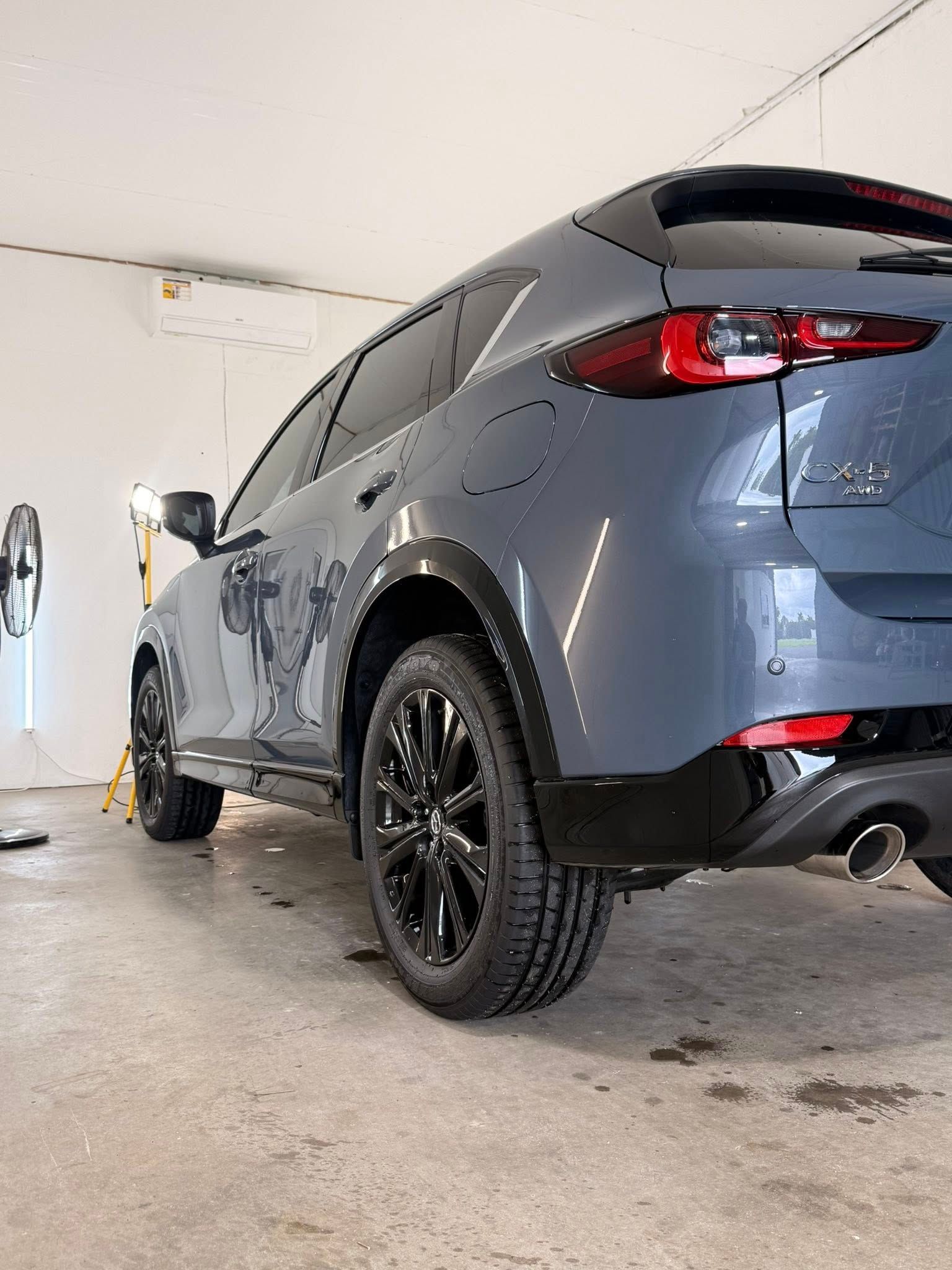 A gray Mazda CX-5 SUV with black wheels parked inside a well-lit garage.