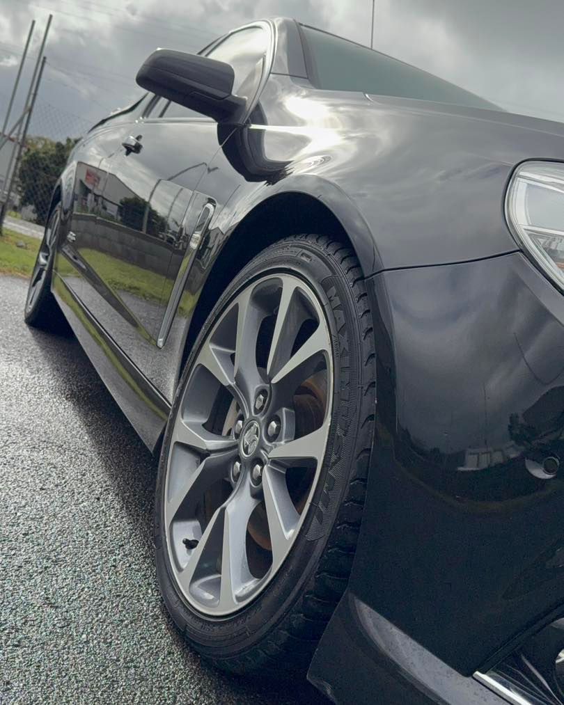 Close-up of a black car’s front side and wheel on a wet road under cloudy skies — Beclean Auto Detailing in Mareeba, QLD