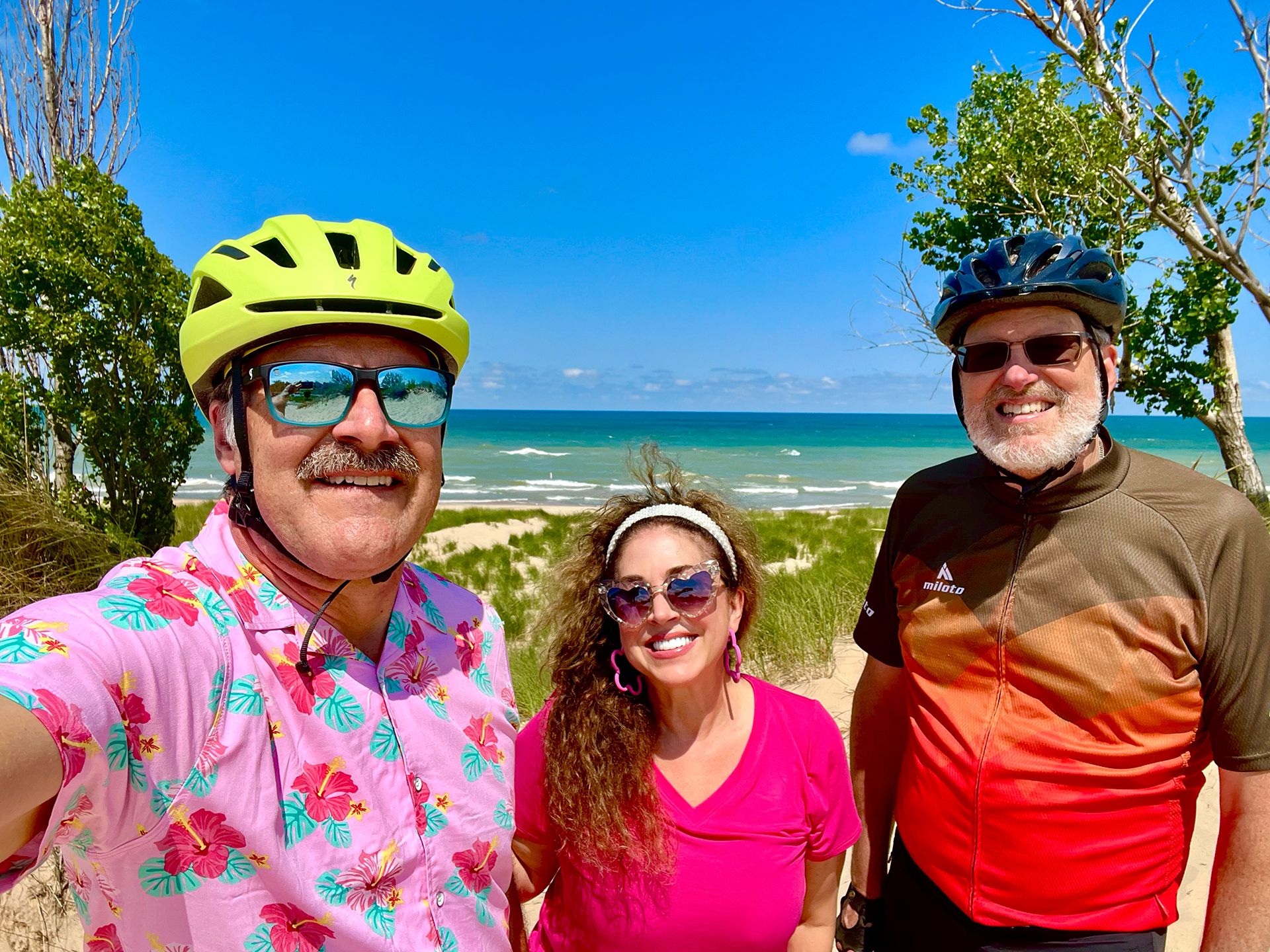 A group of people are standing next to each other on a beach with bike helmets on