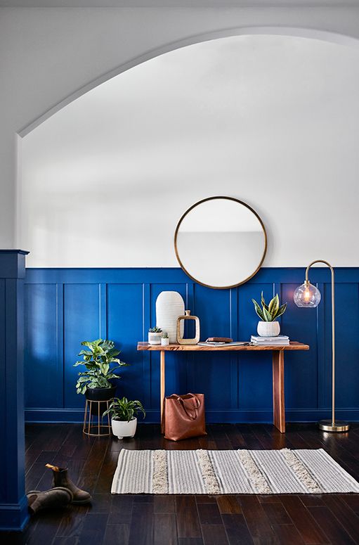 A living room with blue walls , a table , a mirror and a rug.