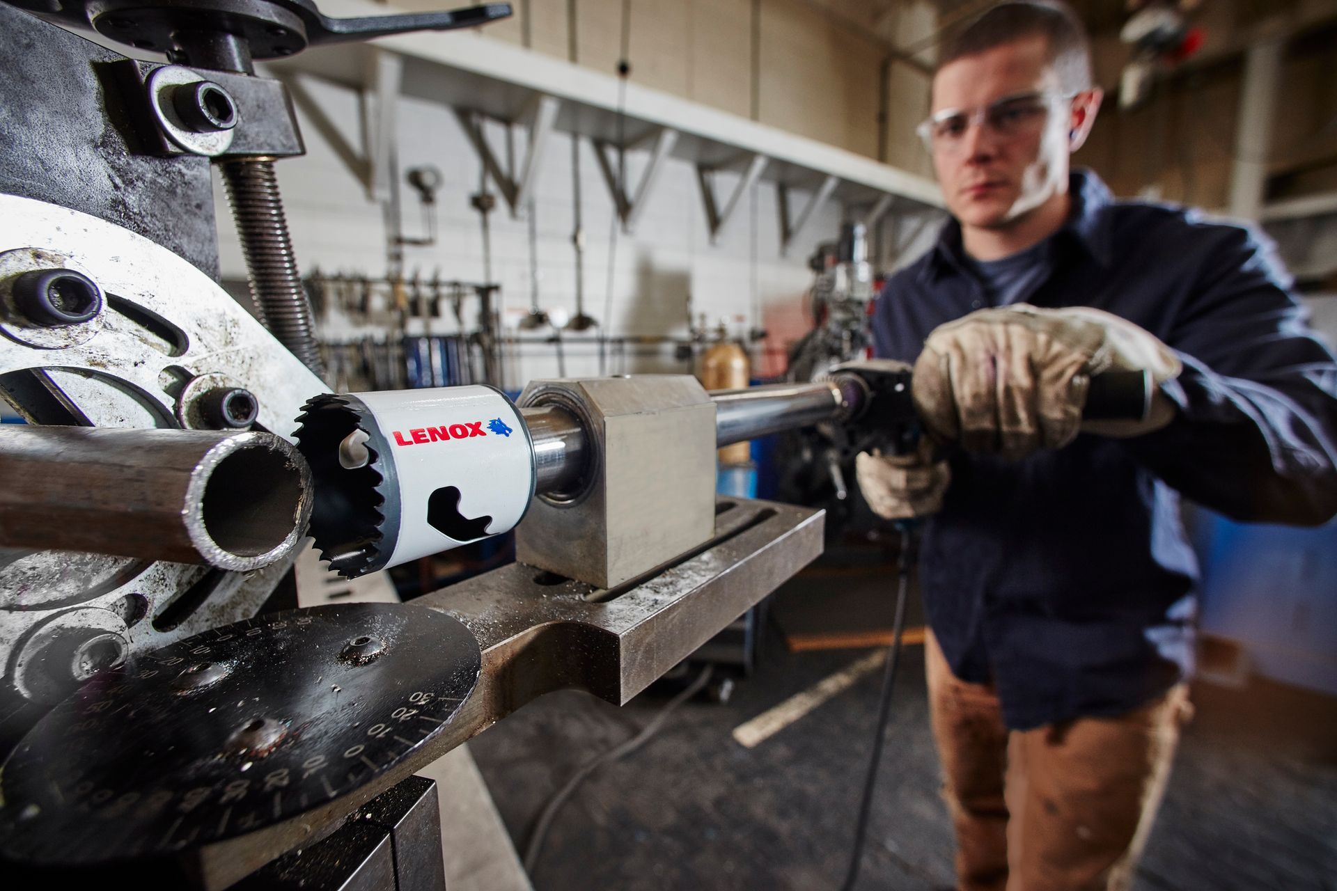 A man is cutting a pipe with a machine in a factory.