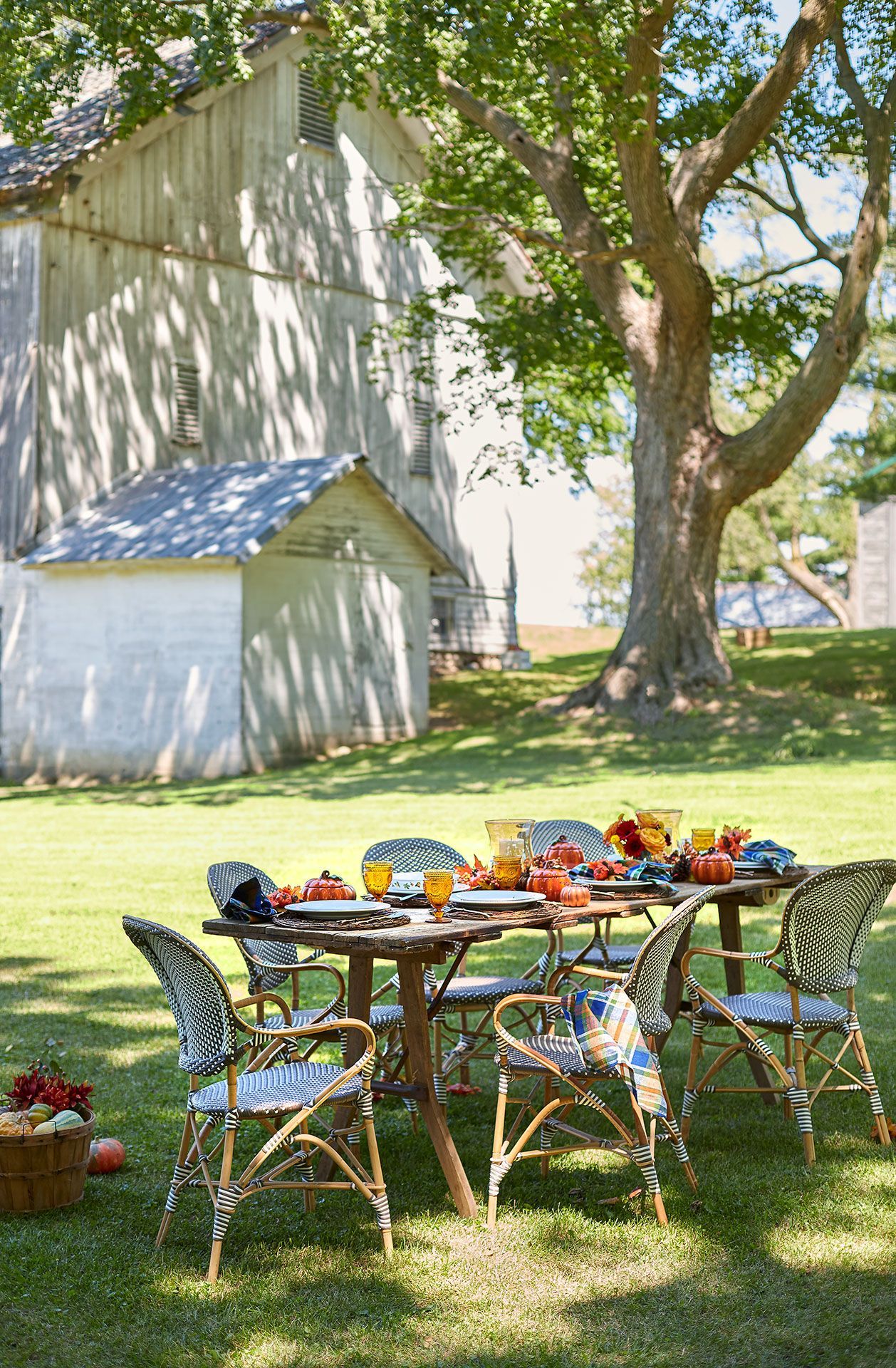 A table and chairs are set up in the grass in front of a barn.