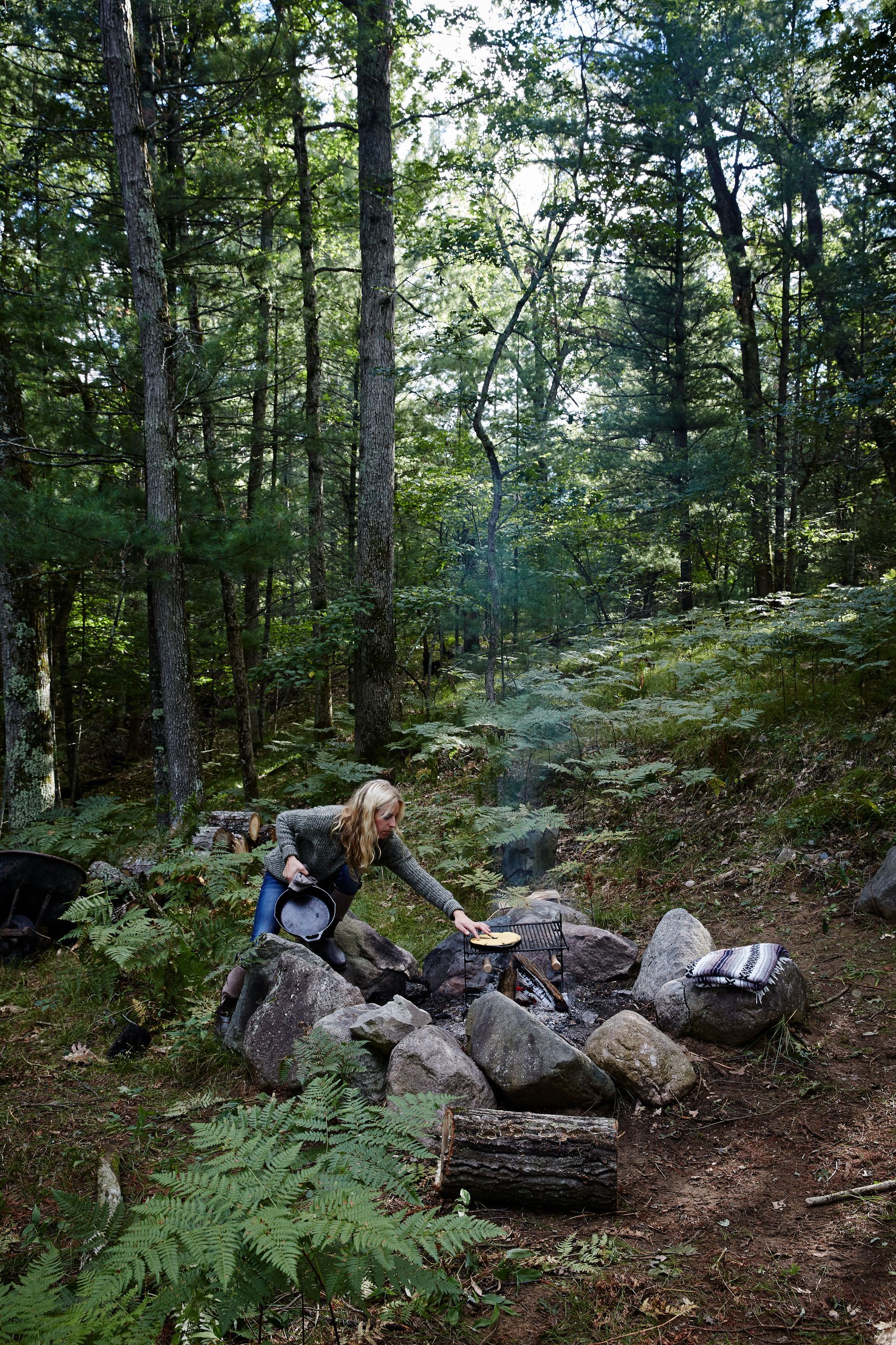 A woman is cooking over a campfire in the woods.