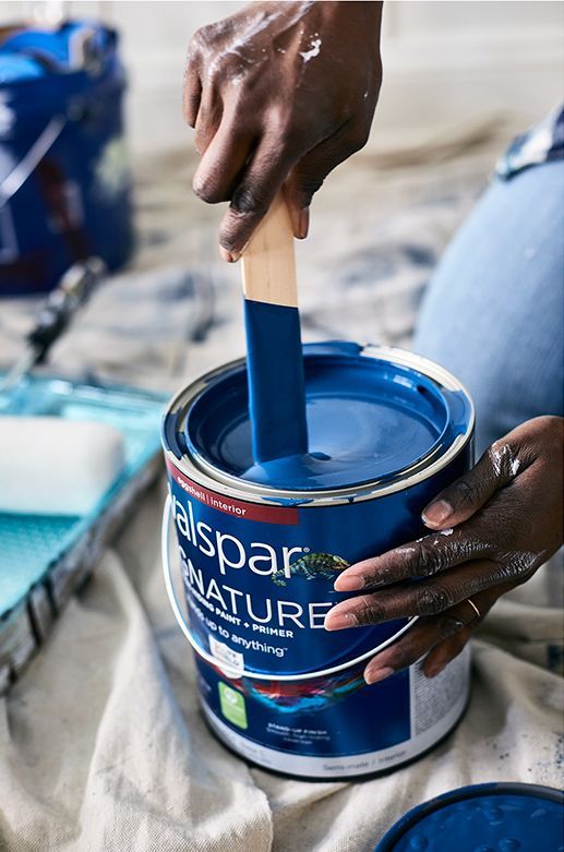 A person is mixing blue paint into a can with a stick