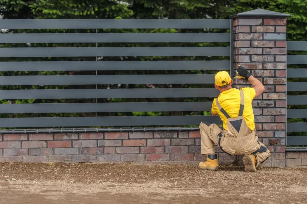 Worker in yellow gear inspecting a brick wall and fence panel outdoors