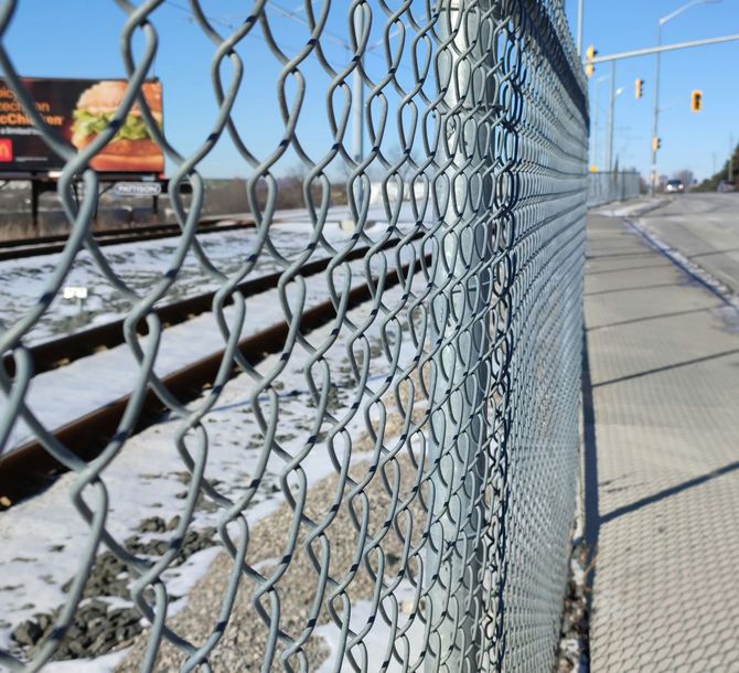 Close-up of a chain-link fence beside a snowy roadside with traffic lights in the distance