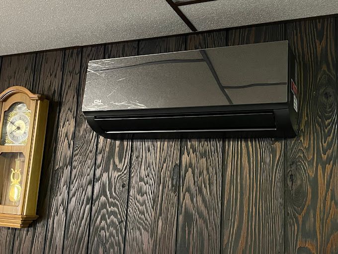 A black air conditioner is hanging on a wooden wall next to a clock.