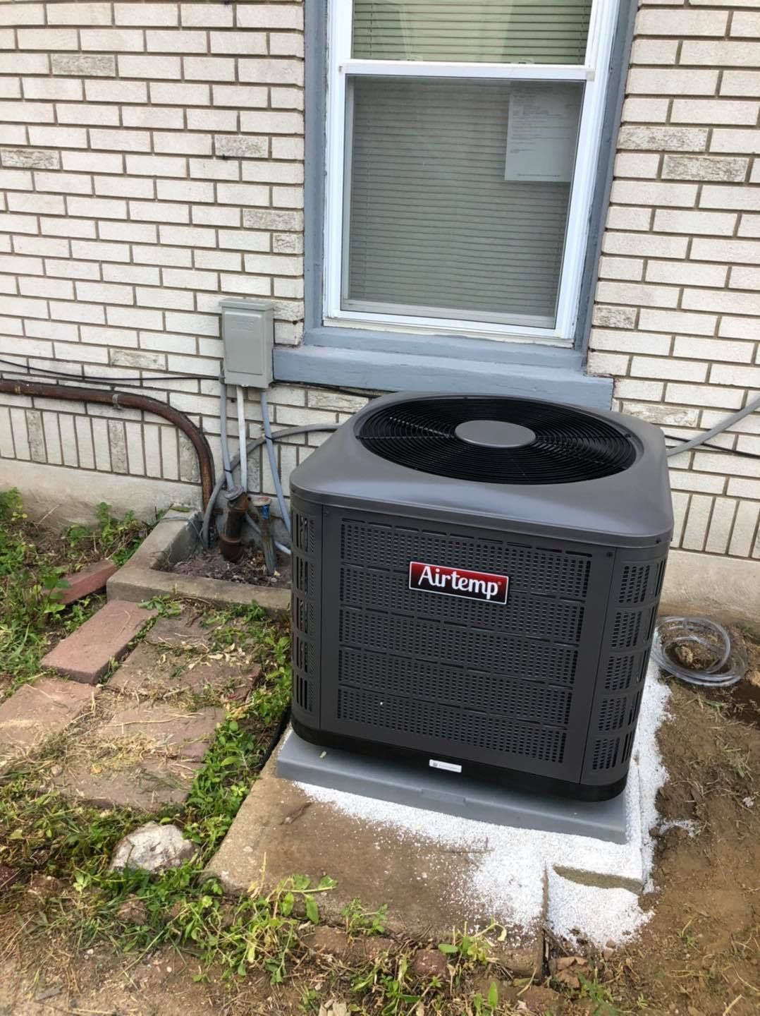 A black air conditioner is sitting in front of a brick building.