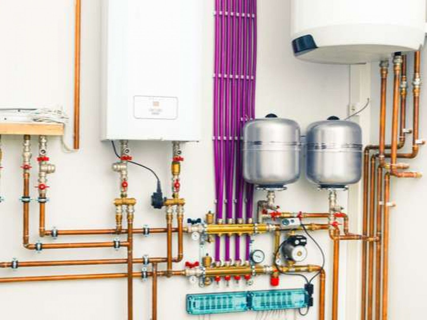 A room with a lot of pipes and a boiler on the wall.
