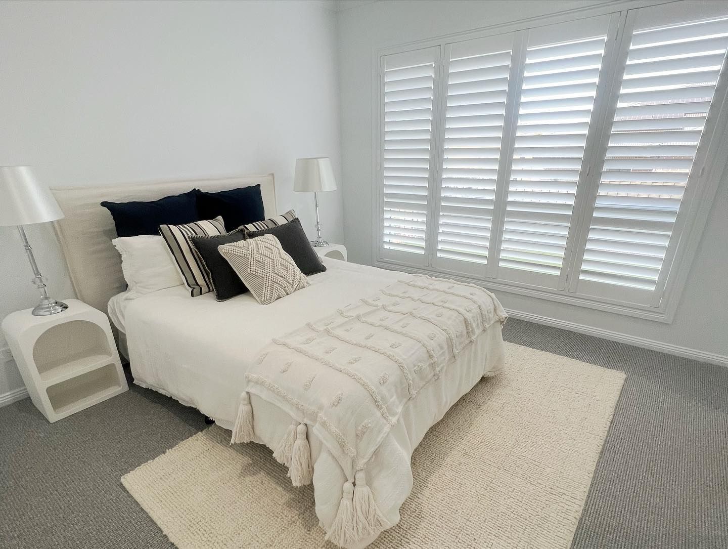A bedroom with a bed , nightstands , and shutters on the windows.