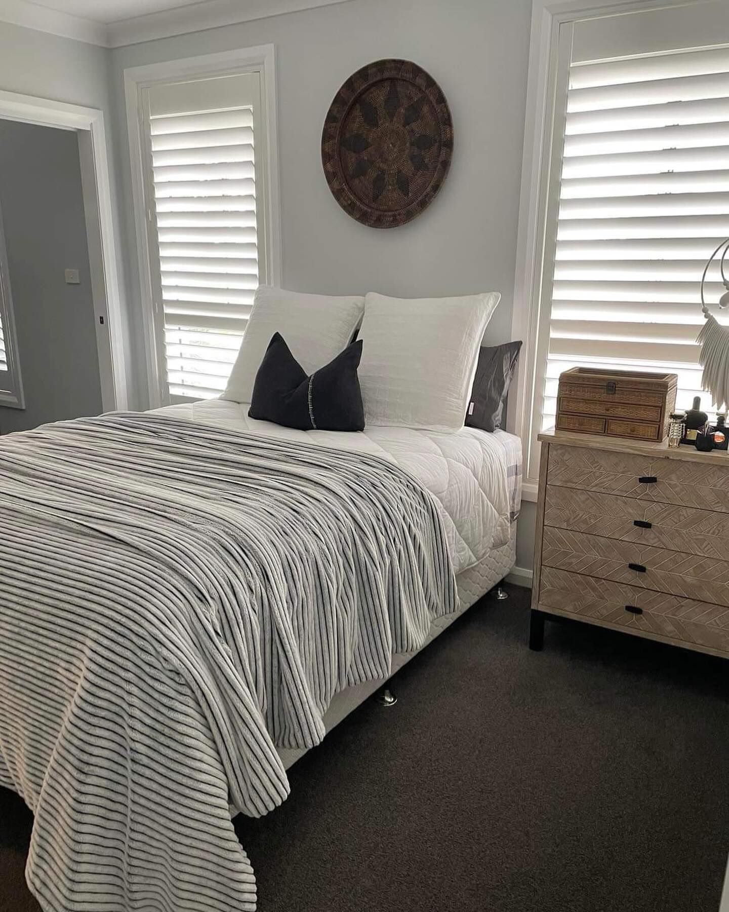 A bedroom with a bed , nightstand , dresser and shutters.